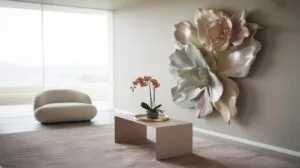 Minimalist living room with a large, sculptural floral wall art, a low table with a potted orchid, a curved cream chair, and floor-to-ceiling windows overlooking a serene outdoor view.